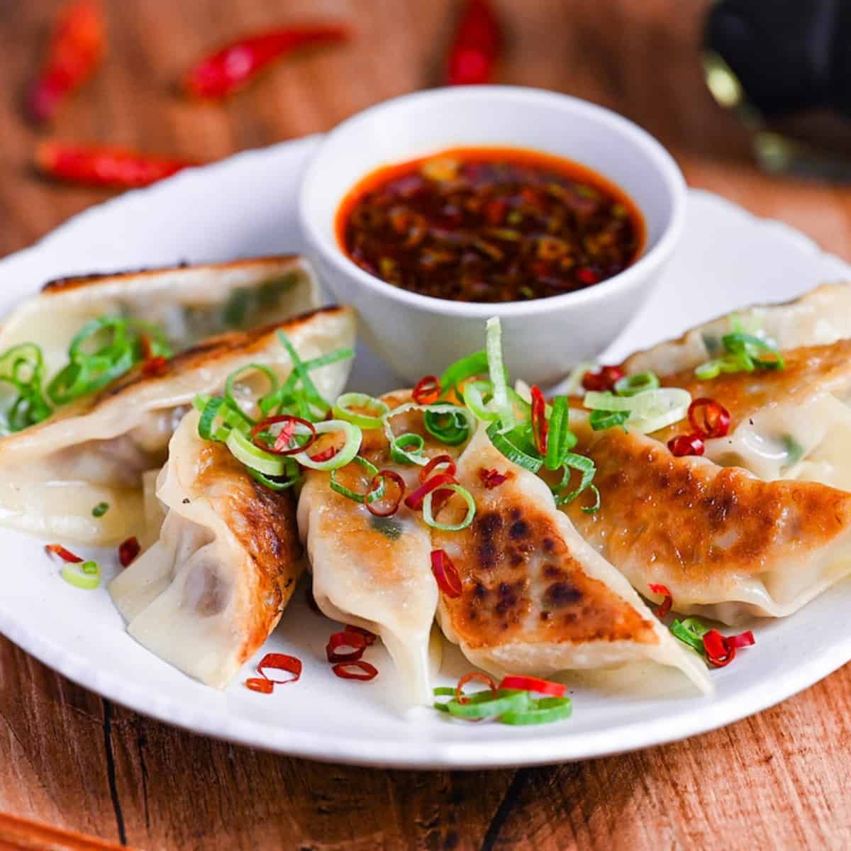 Spicy beef gyoza with hot dipping sauce sprinkled with chopped green onion and dry chilis on a white plate