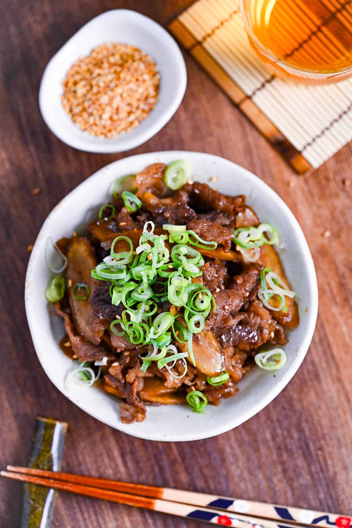 Beef shigureni with ginger and burdock root in a white dish topped with chopped green onion
