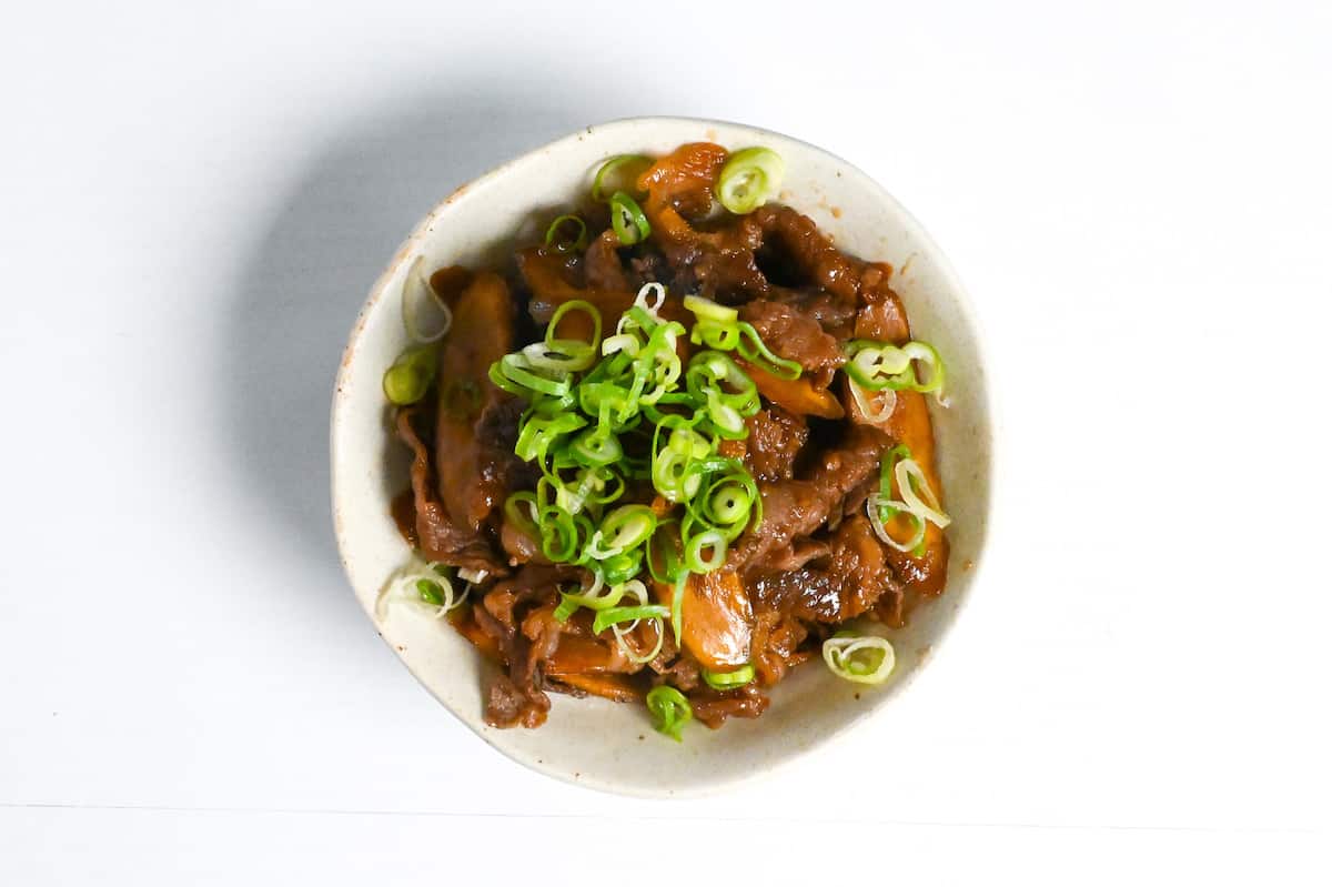 Beef shigureni with ginger and burdock root in a white dish topped with chopped green onion