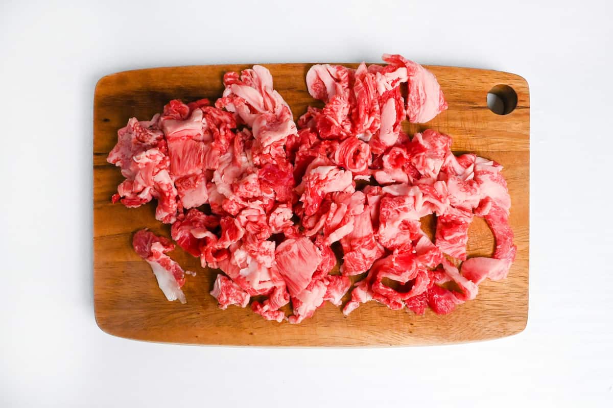 thinly sliced wagyu beef cut into 2cm pieces on a wooden chopping board