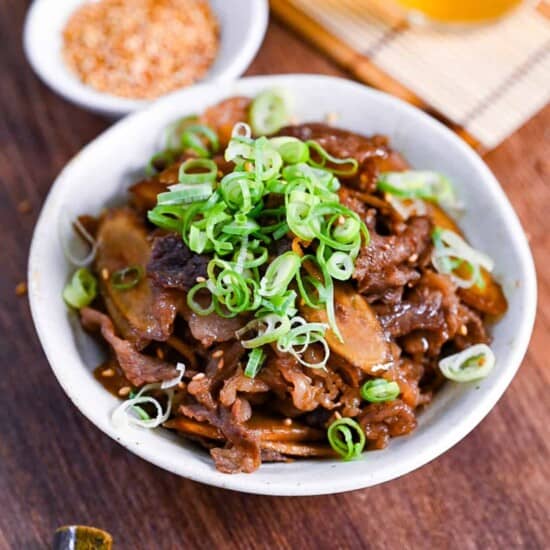 Beef shigureni with ginger and burdock root in a white dish topped with chopped green onion