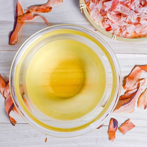 Katsuo (bonito flake) dashi in a glass bowl surrounded by bonito flakes
