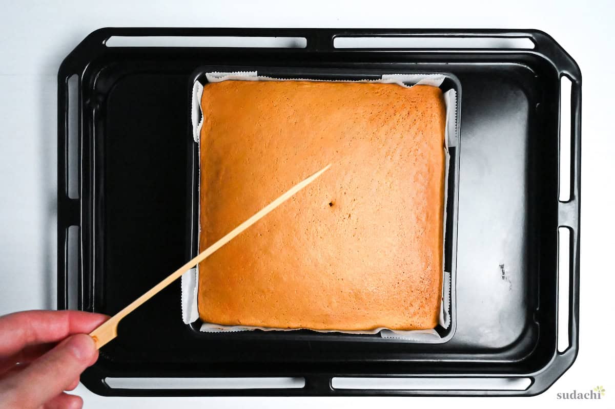 baked castella cake on a baking tray pierced with a skewer to check it's cooked through