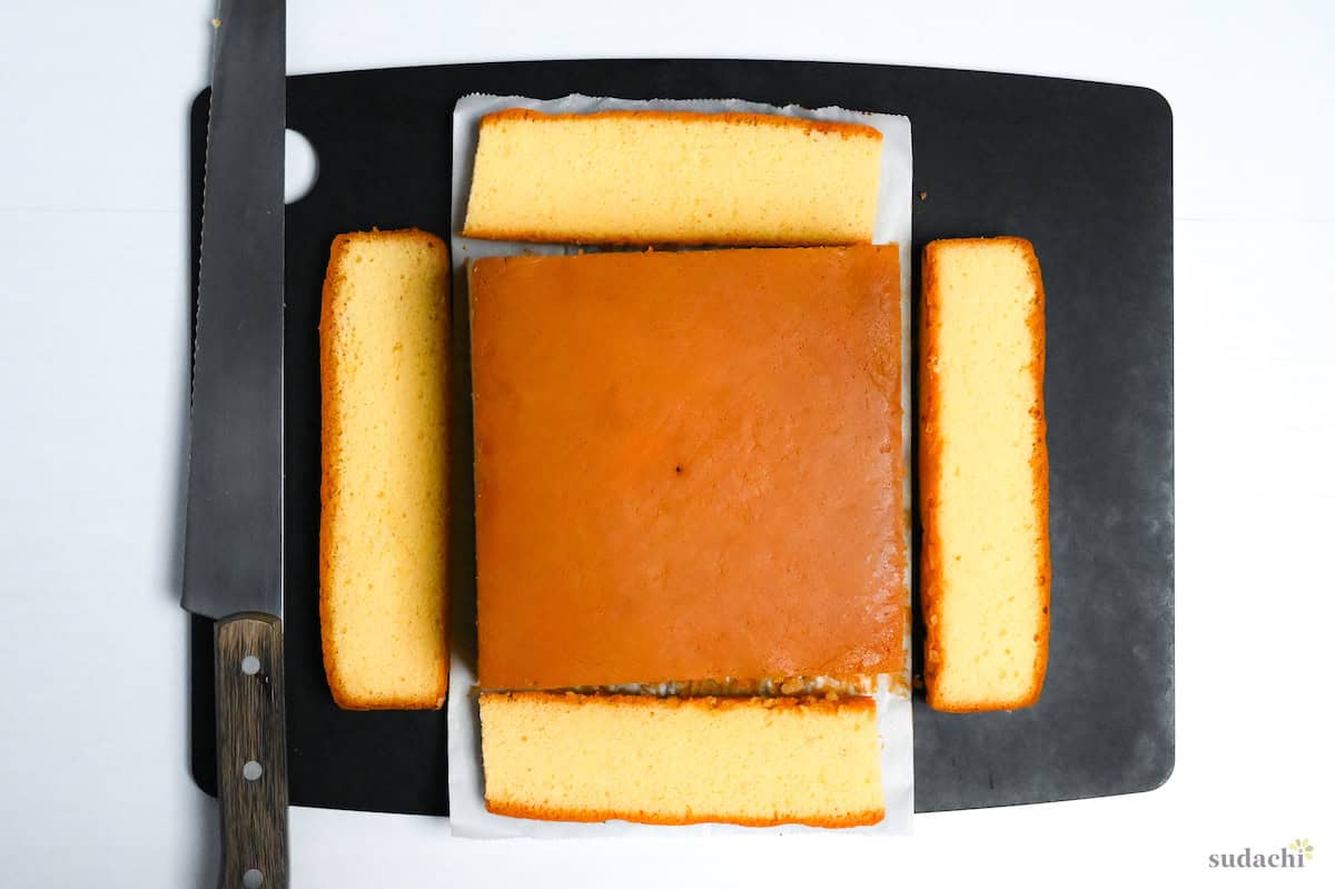 cooled castella on a black chopping board with edges cut off