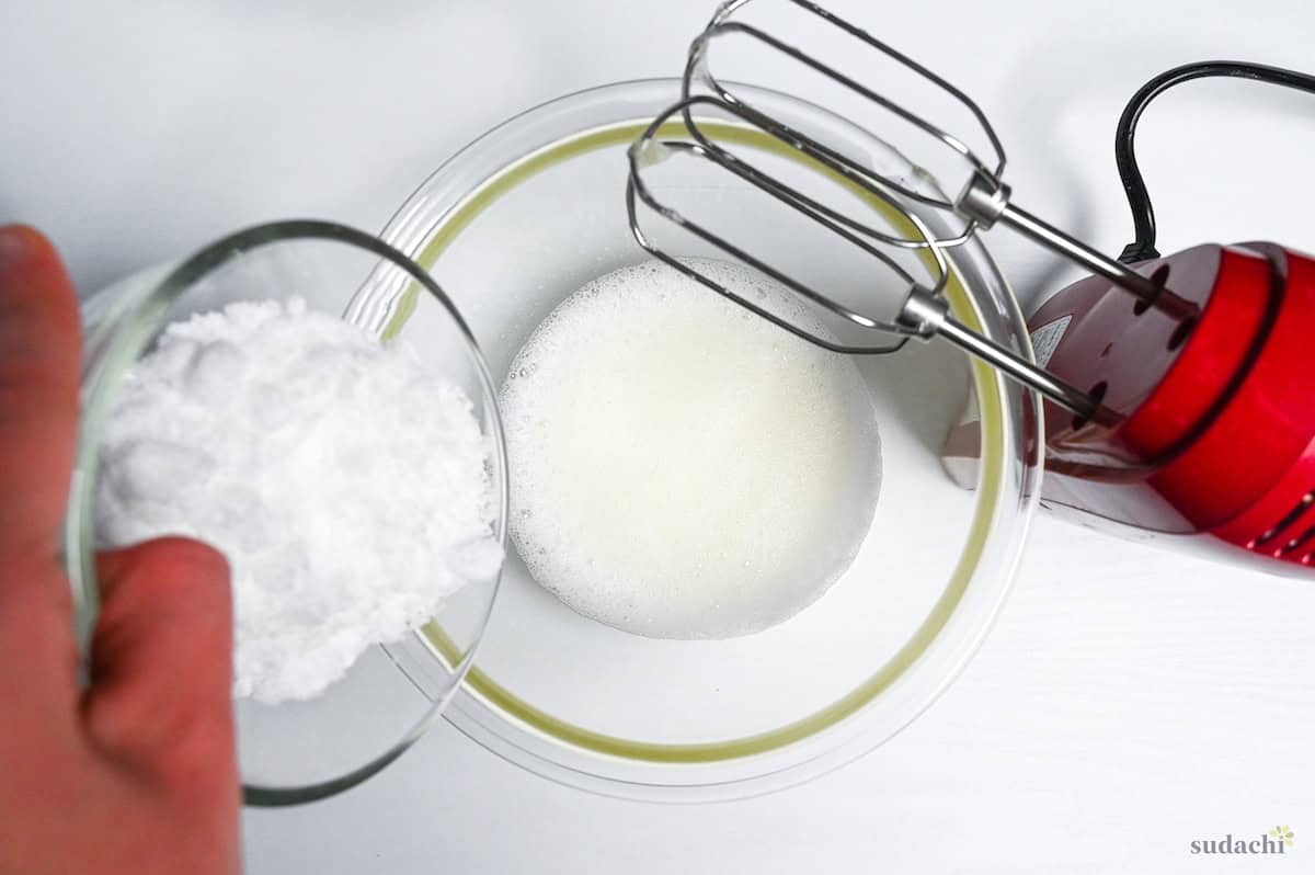 whisking egg whites in a glass mixing bowl and gradually adding white sugar