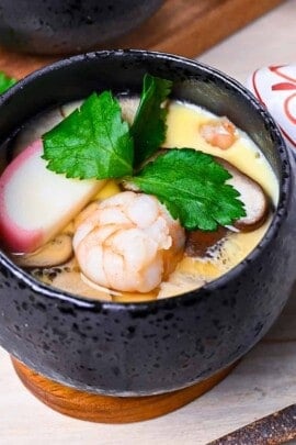 Chawanmushi (Japanese steamed egg custard) in black steaming cups with white and red decorative lids