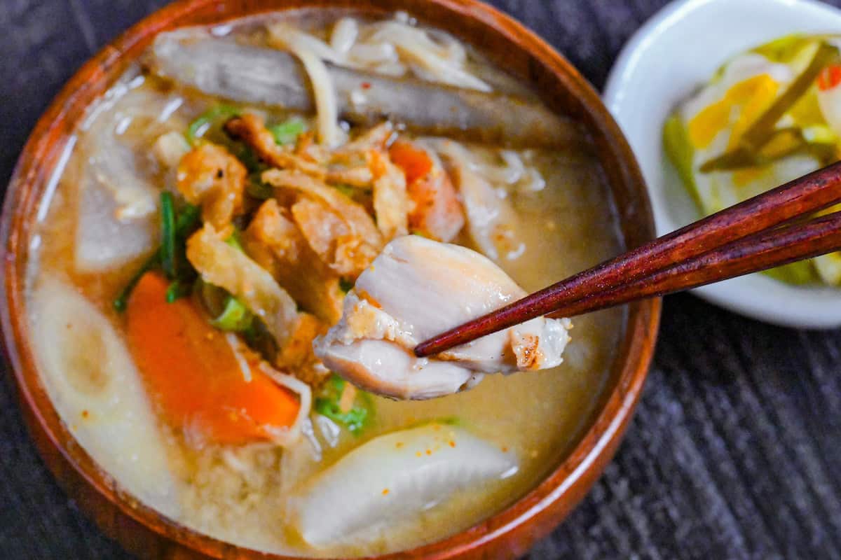 holding a piece of chicken from torijiru with wooden chopsticks