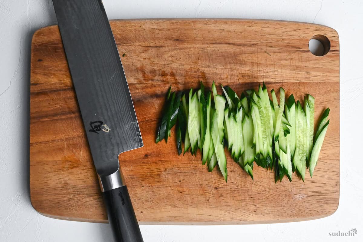 julienned cucumber with vegetable knife on a wooden cutting board