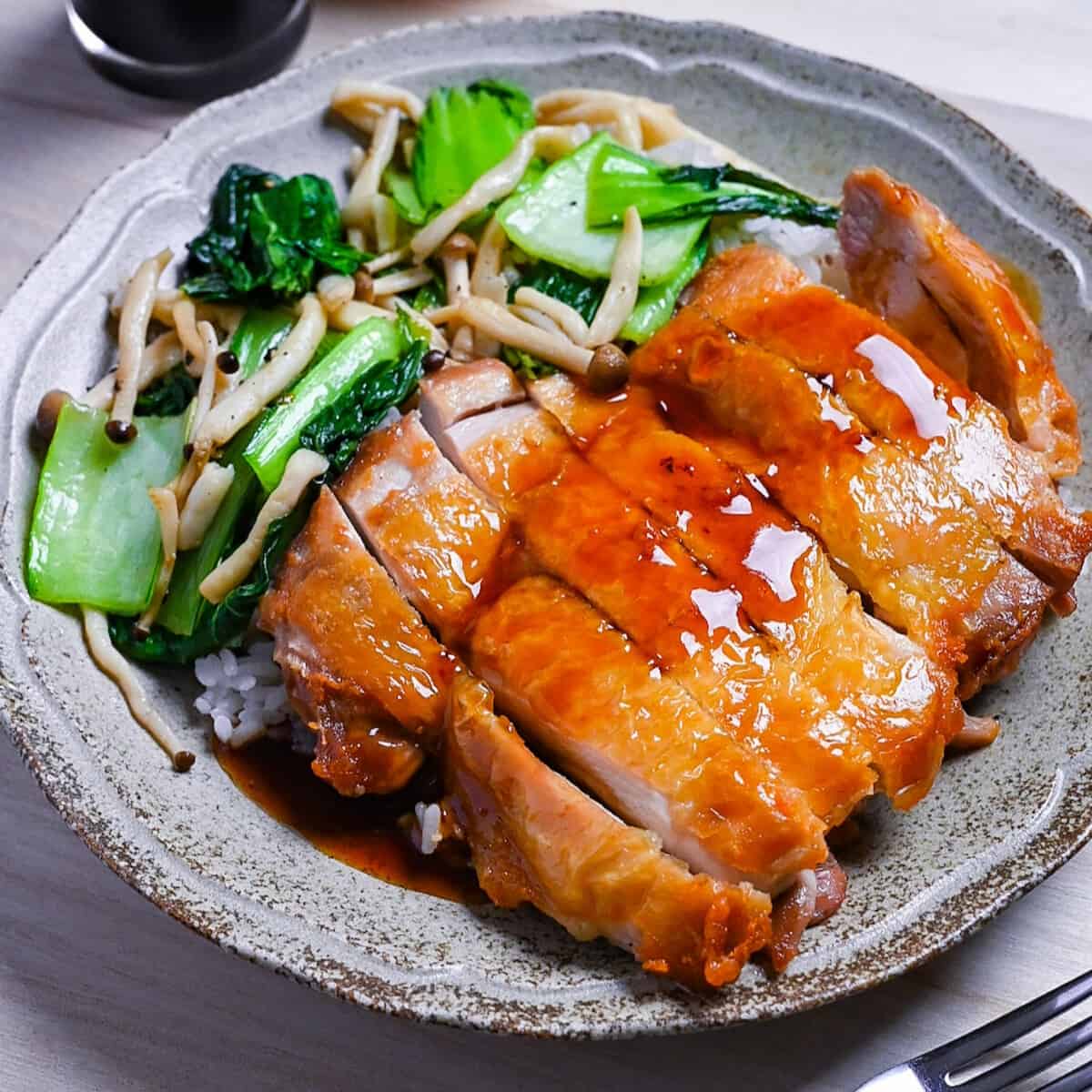 Crispy chicken steak drizzled with ponzu sauce served with rice and sautéed vegetables on a beige plate