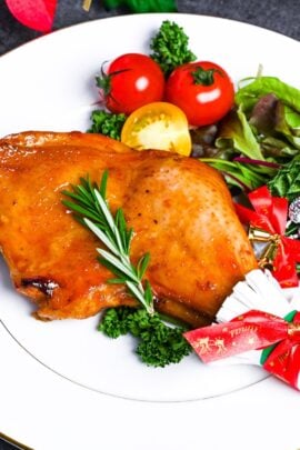Japanese Christmas Chicken (Roasted Chicken with Soy and Yuzu Glaze) on a white plate topped with a sprig of fresh rosemary next to a simple side salad