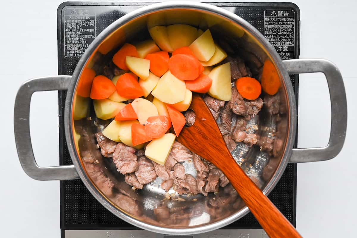Potatoes and carrots added to a pot with beef