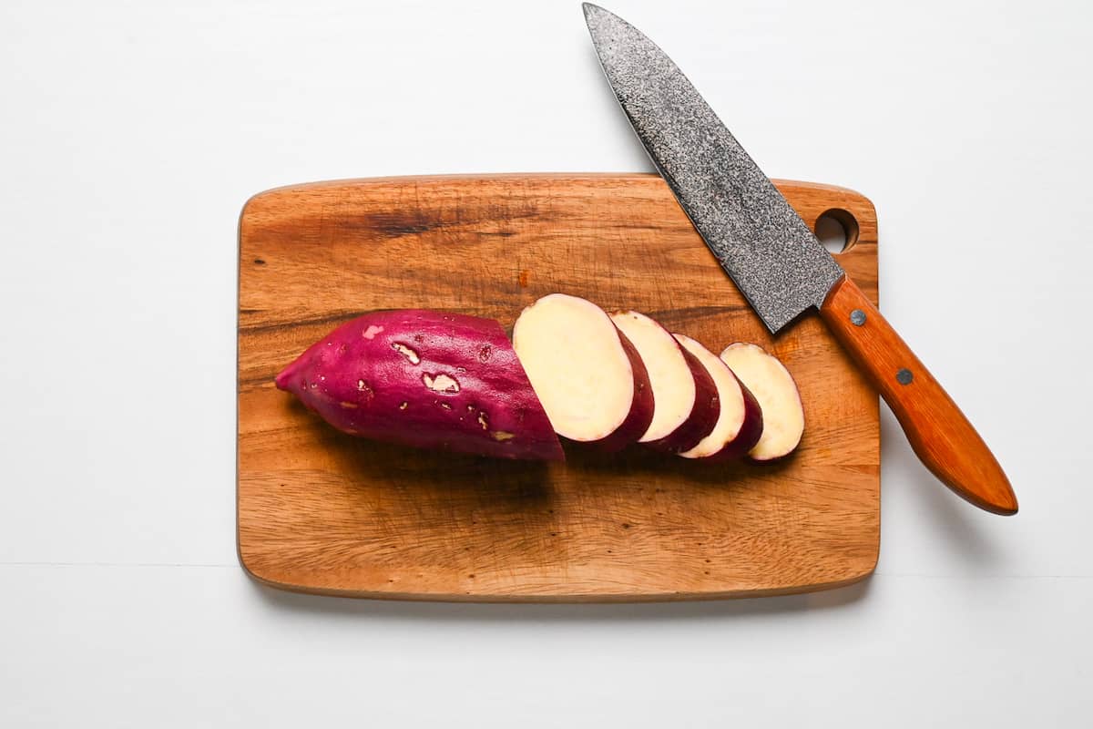 Japanese sweet potato cut into thick rounds on a wooden chopping board