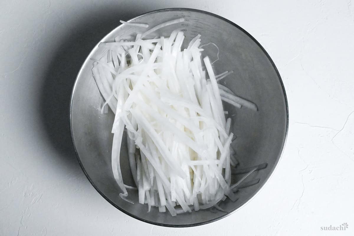 julienned daikon radish in a mixing bowl with salt