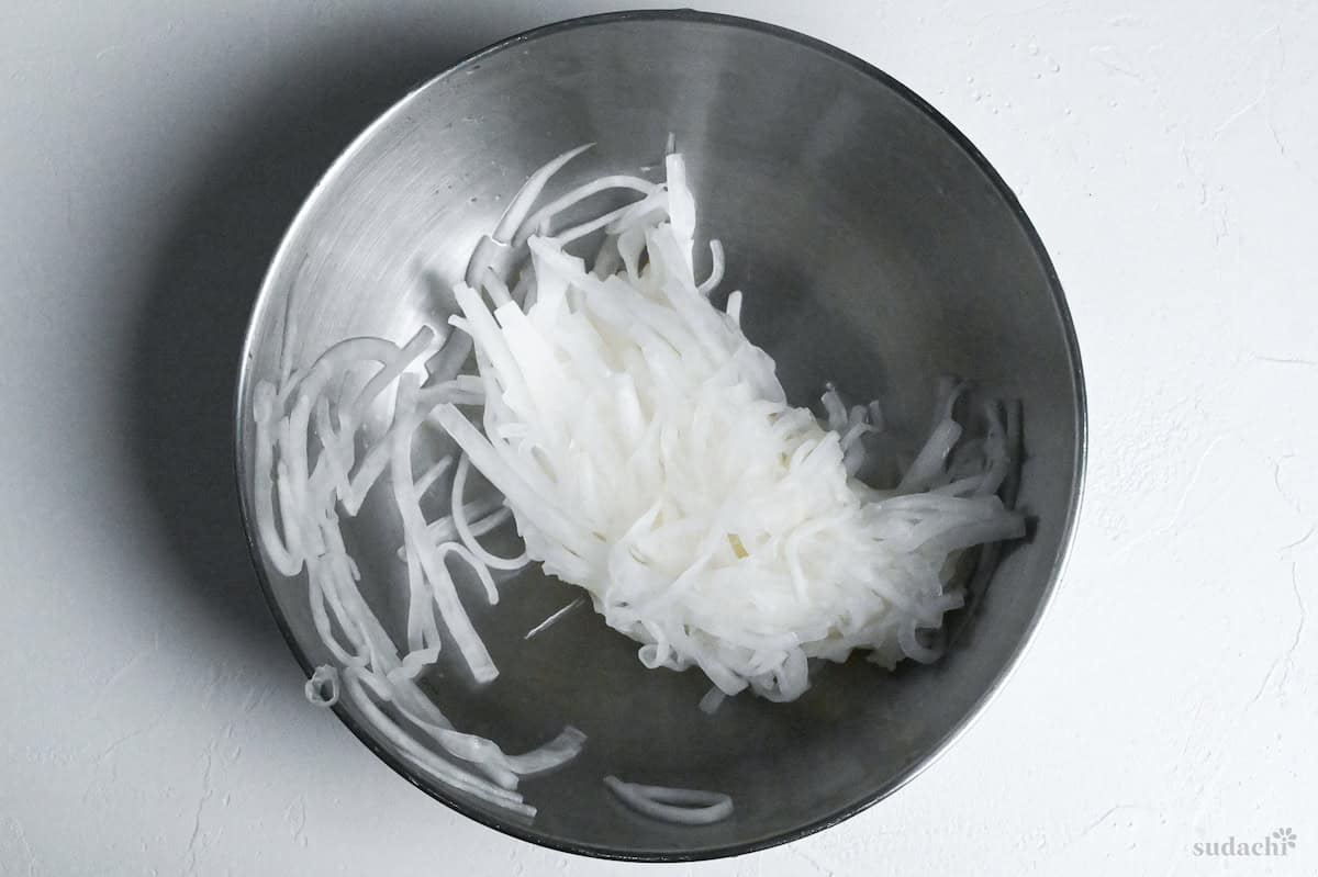 squeezed daikon radish in a steel mixing bowl on a white background