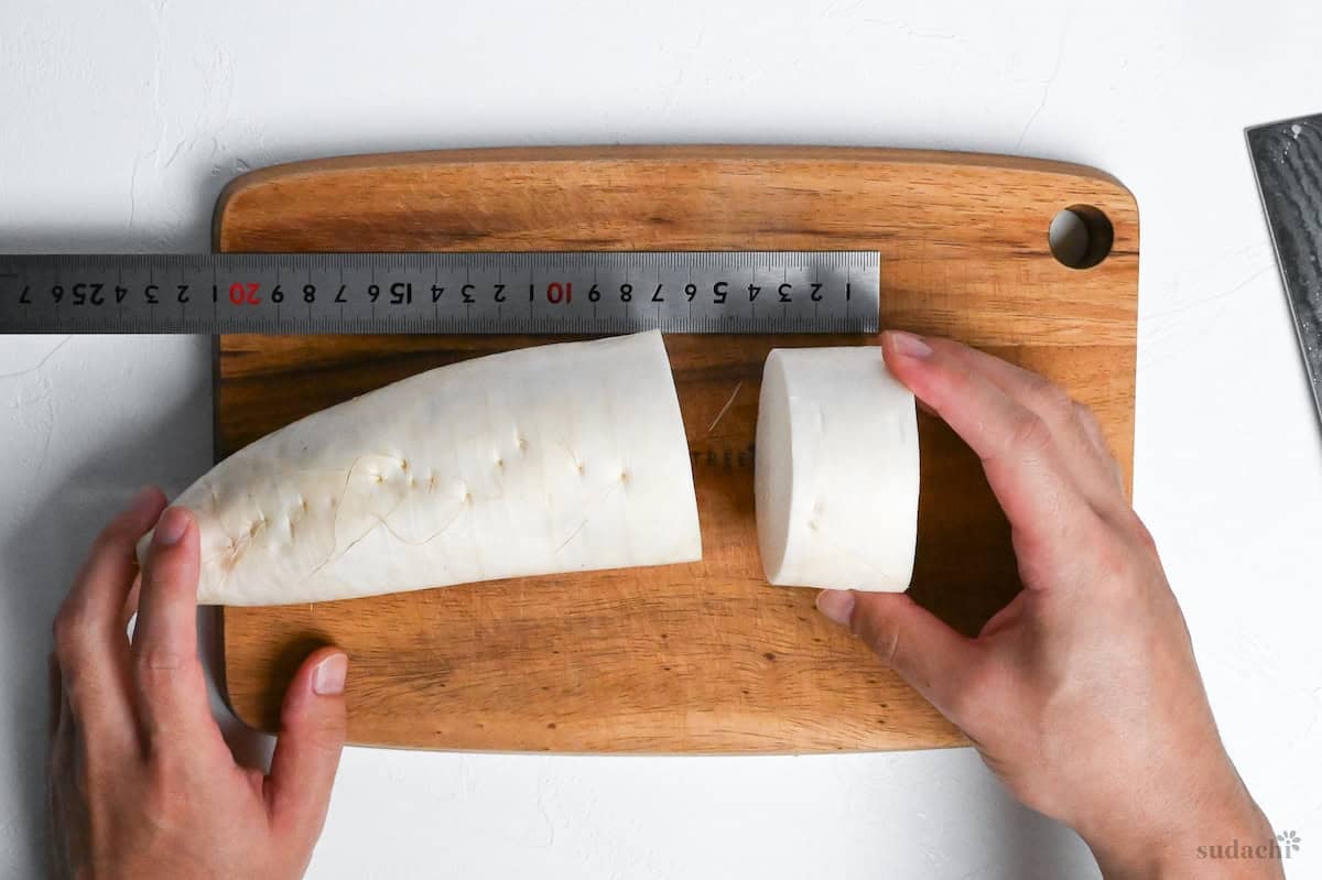 Cutting daikon radish into 3.5cm thick rounds on a wooden cutting board