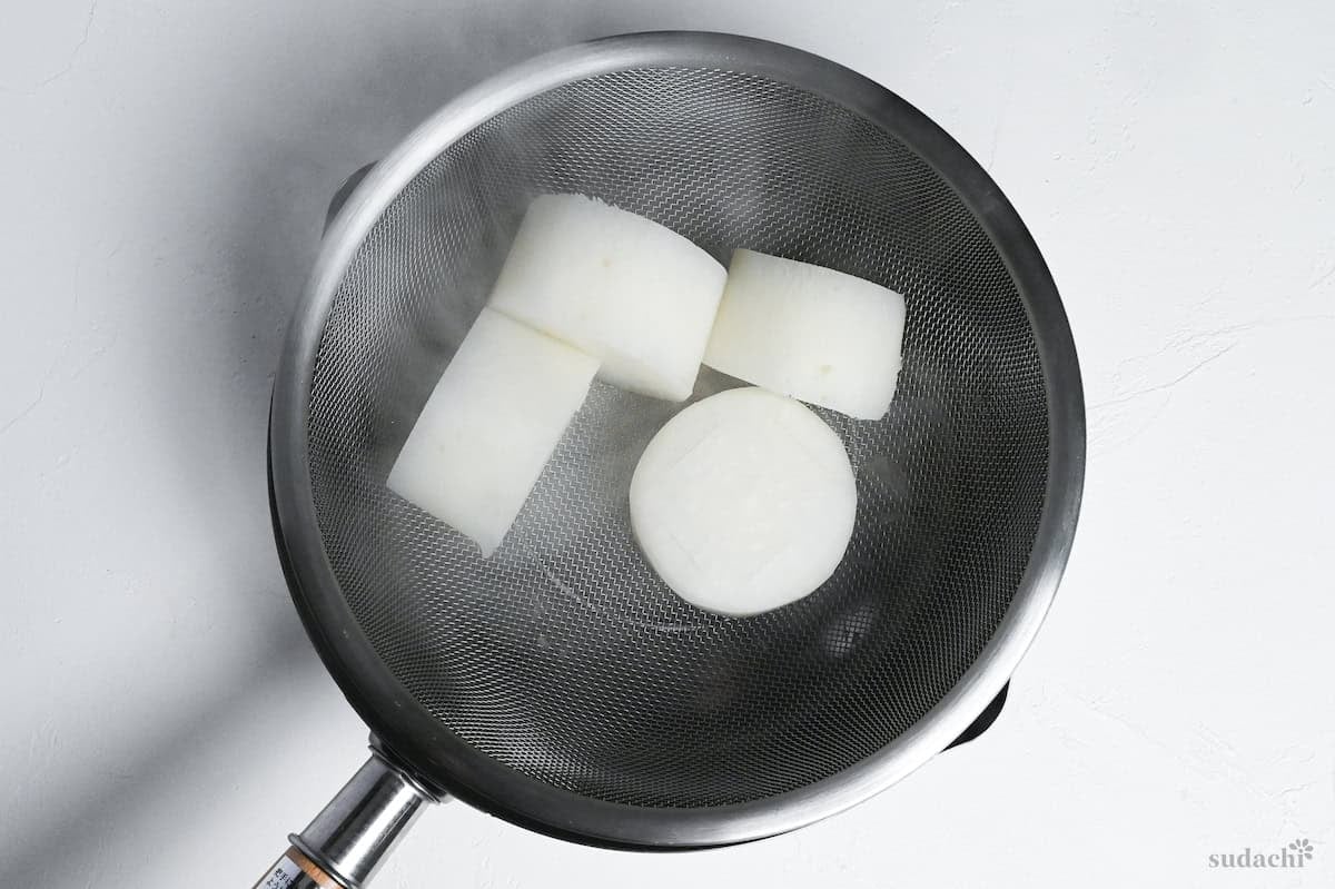 drained daikon rounds in a wire mesh sieve over a pot