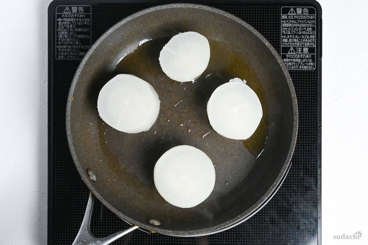 pre-boiled daikon rounds frying in a pan with oil