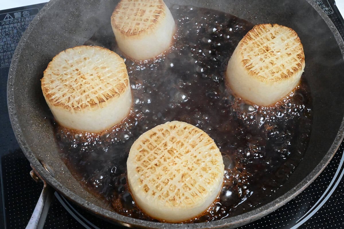 boiled and fried daikon rounds in a pan with sauce close up