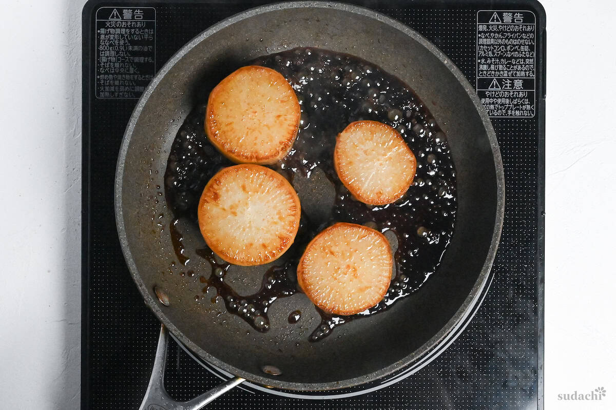 Daikon rounds frying in a pan with sauce