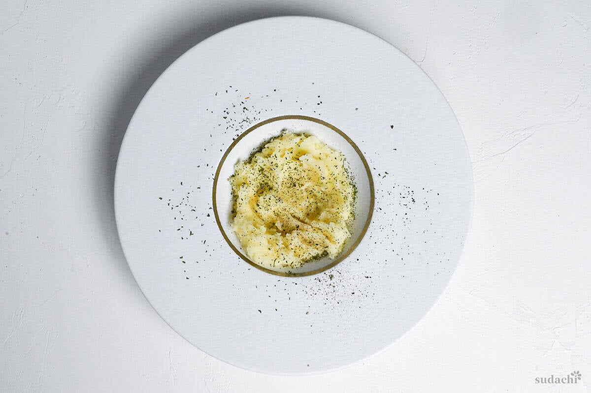 White plate with mashed potato sprinkled with dry parsley and ground black pepper