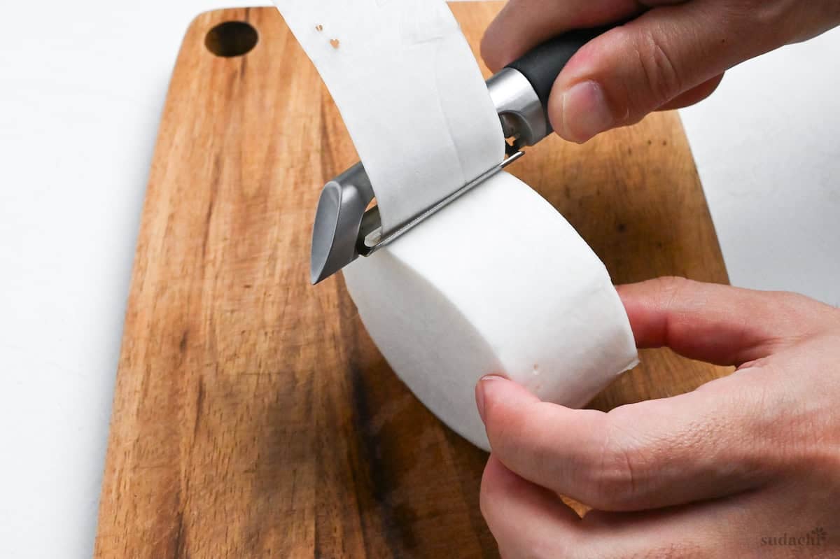 close up of peeling the outer skin of daikon radish with a vegetable peeler