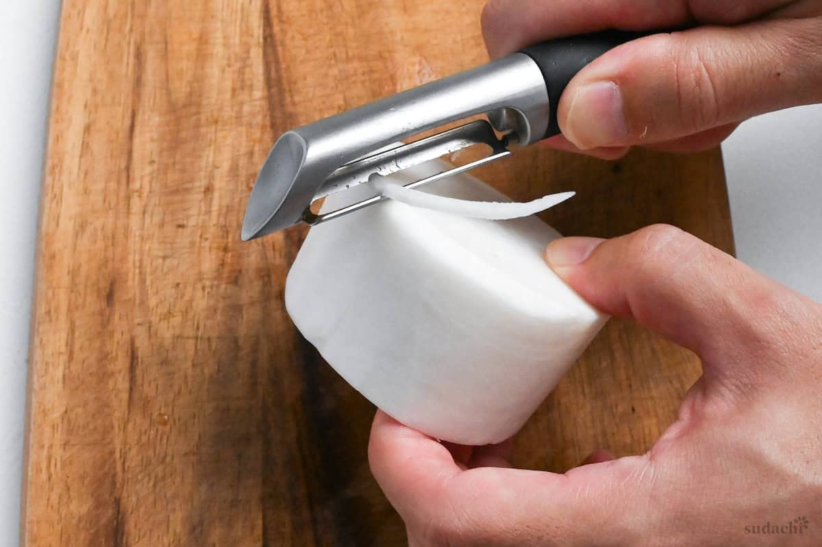 peeling the edge of a daikon radish round with a vegetable peeler close up