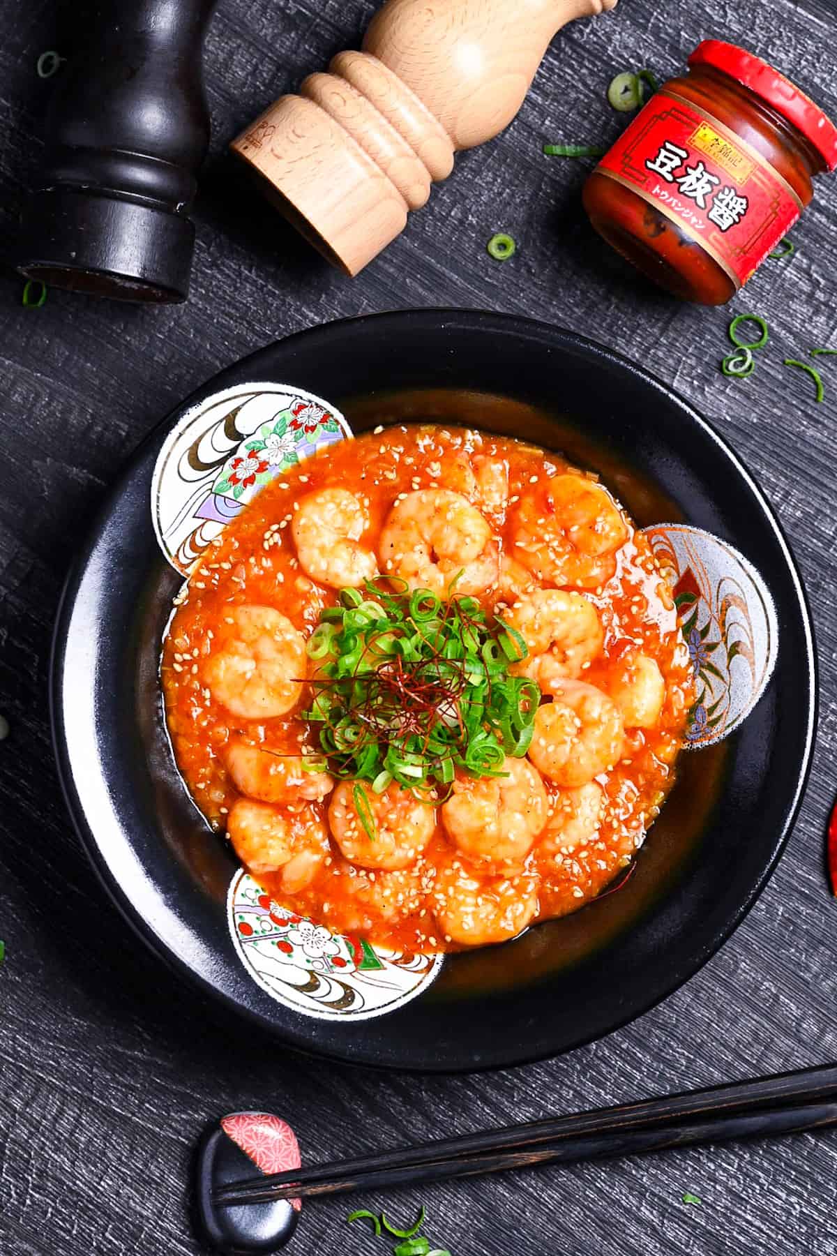 ebi chili in a black bowl sprinkled with finely chopped green onion, sesame seeds and chili threads