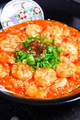 ebi chili in a black bowl sprinkled with finely chopped green onion, sesame seeds and chili threads