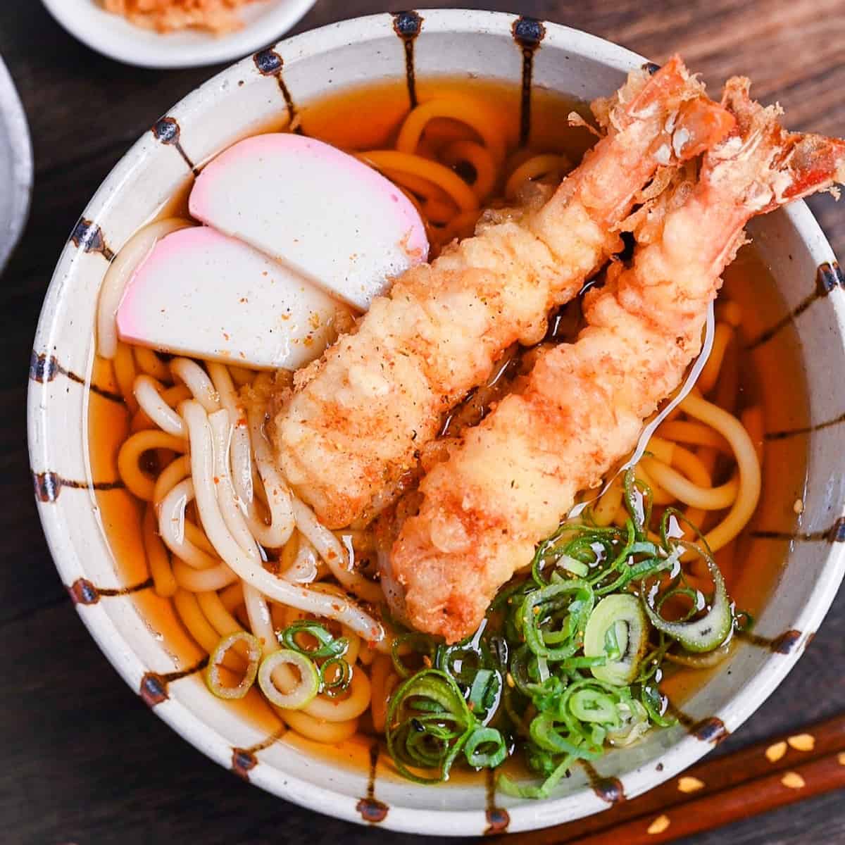 Ebiten Udon - Homemade udon noodle soup in a stripy bowl topped with kamaboko, green onion and tempura shrimp
