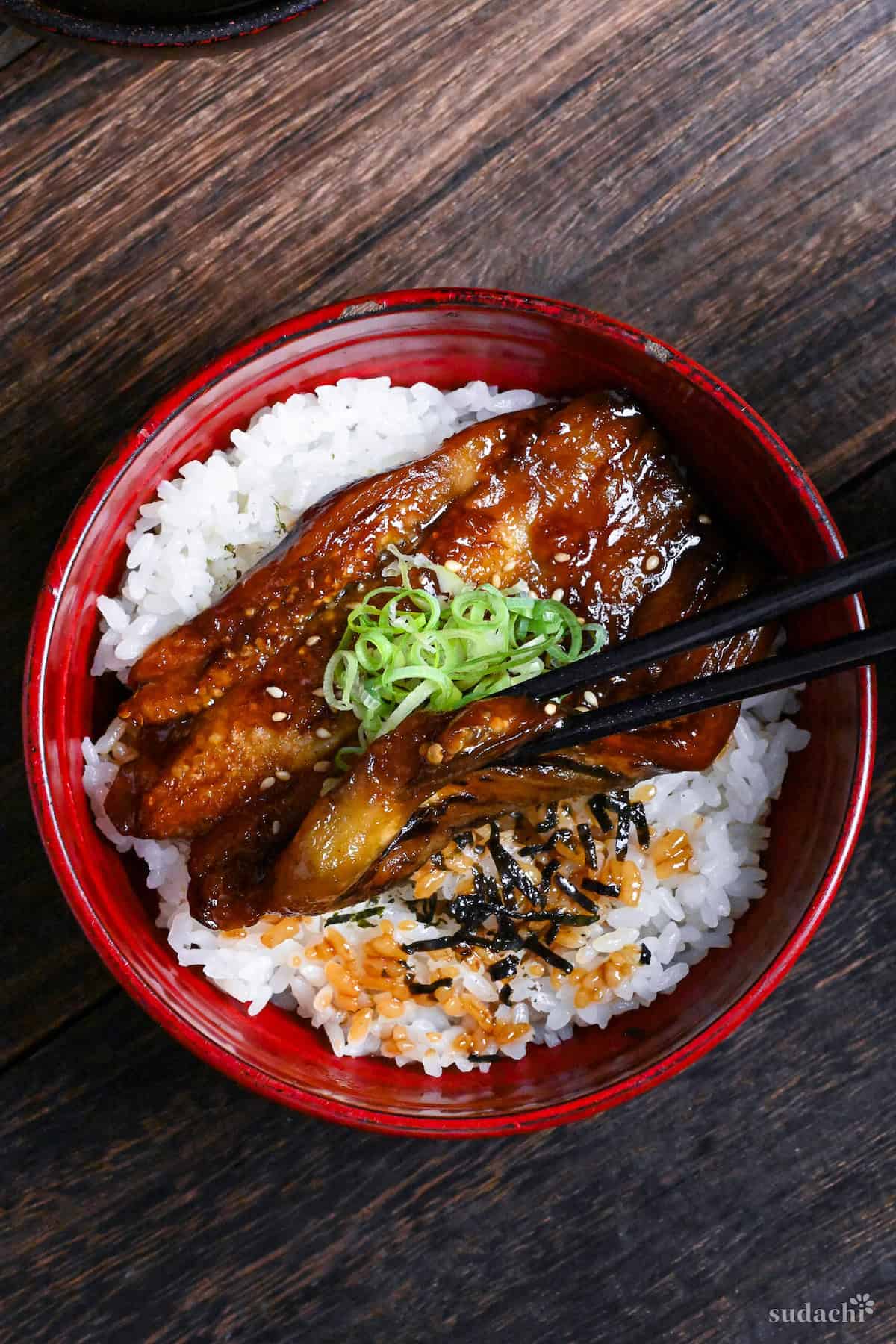 eel kabayaki in a red bowl on a dark wooden surface top down view