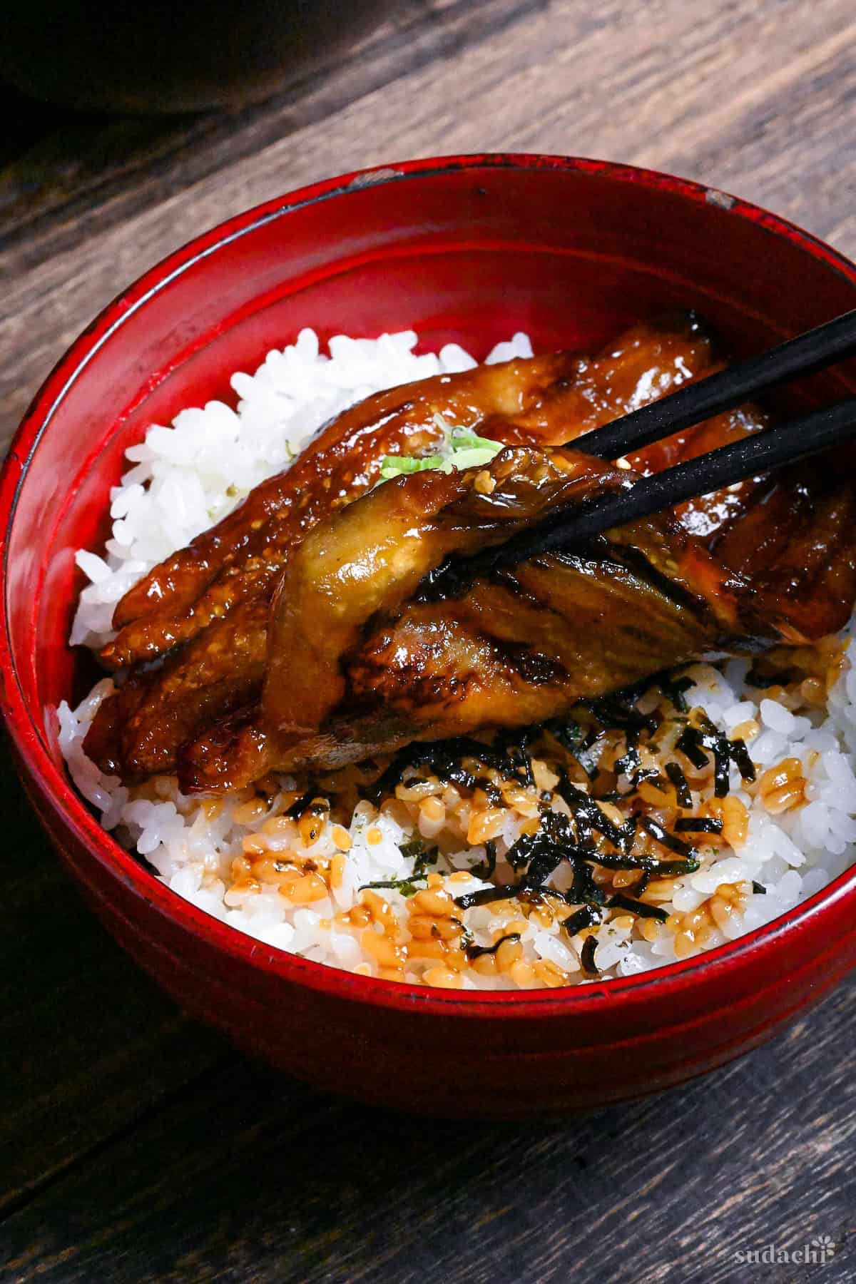 eel kabayaki in a red bowl on a dark wooden surface