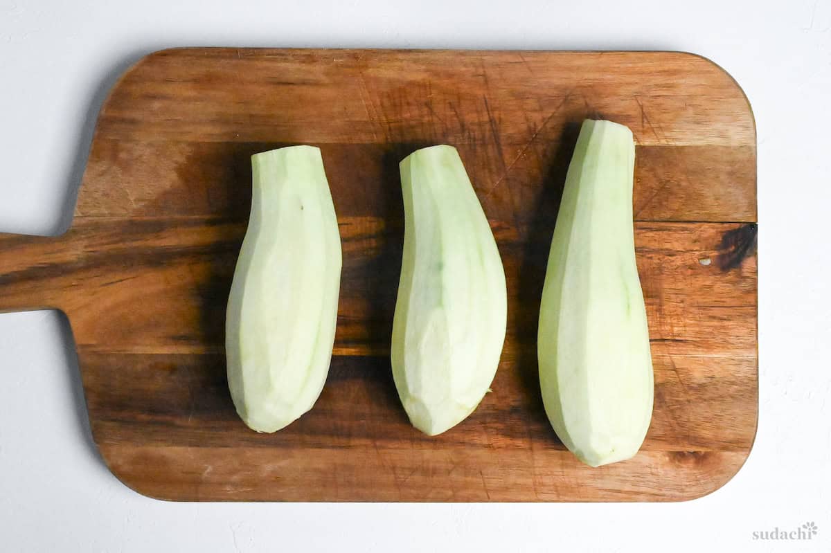 three peeled eggplants on a wooden chopping board