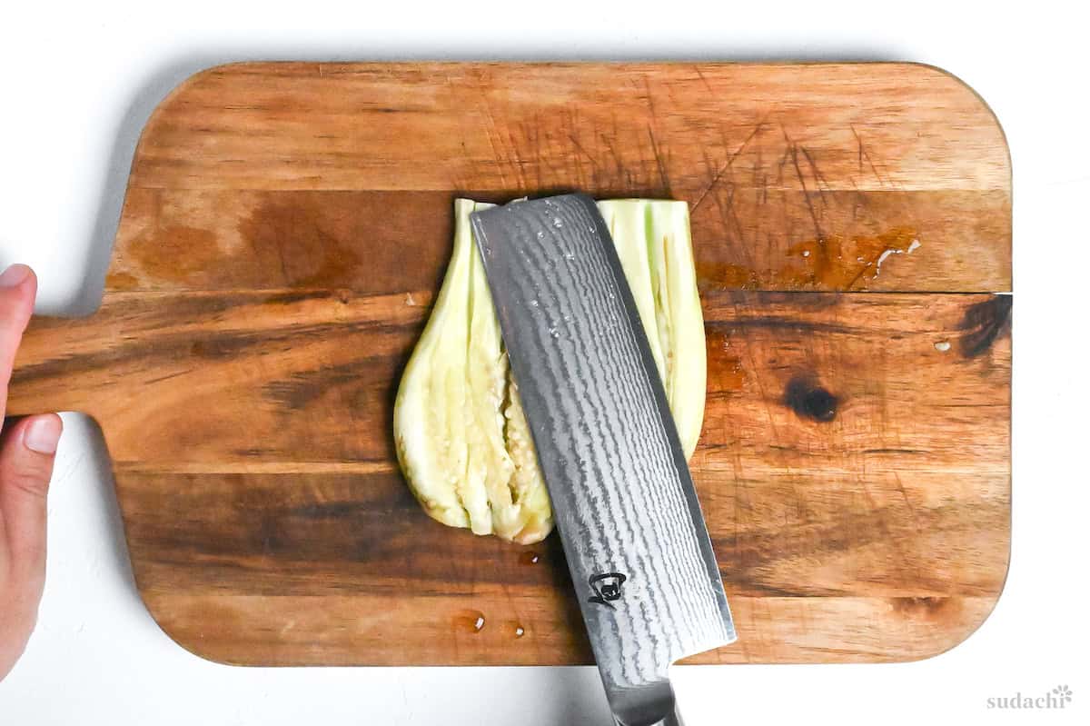 flattening butterflied eggplant on a wooden chopping board with a large Japanese vegetable knife
