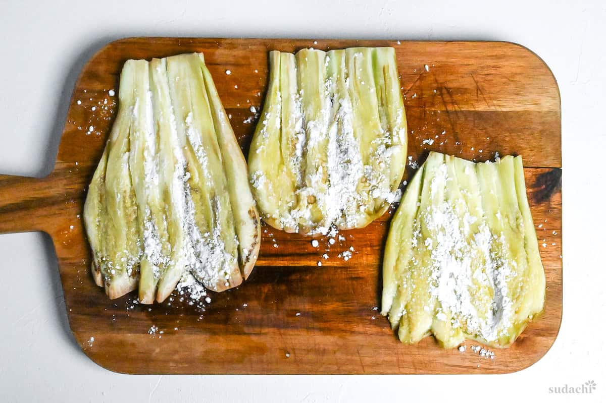 butterflied eggplants sprinkled with flour on a wooden chopping board