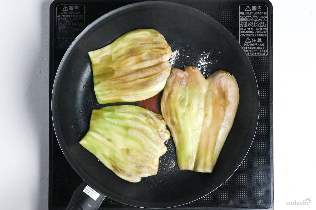 butterflied eggplants frying in an oil frying pan