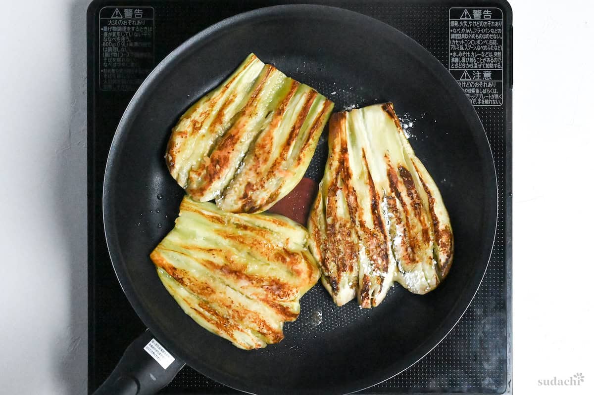 frying butterflied eggplants in an oiled frying pan on the stove