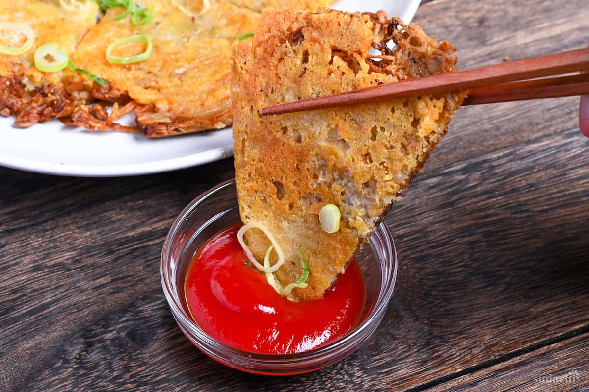Dipping a triangular piece of crispy enoki cheese into small glass bowl of ketchup