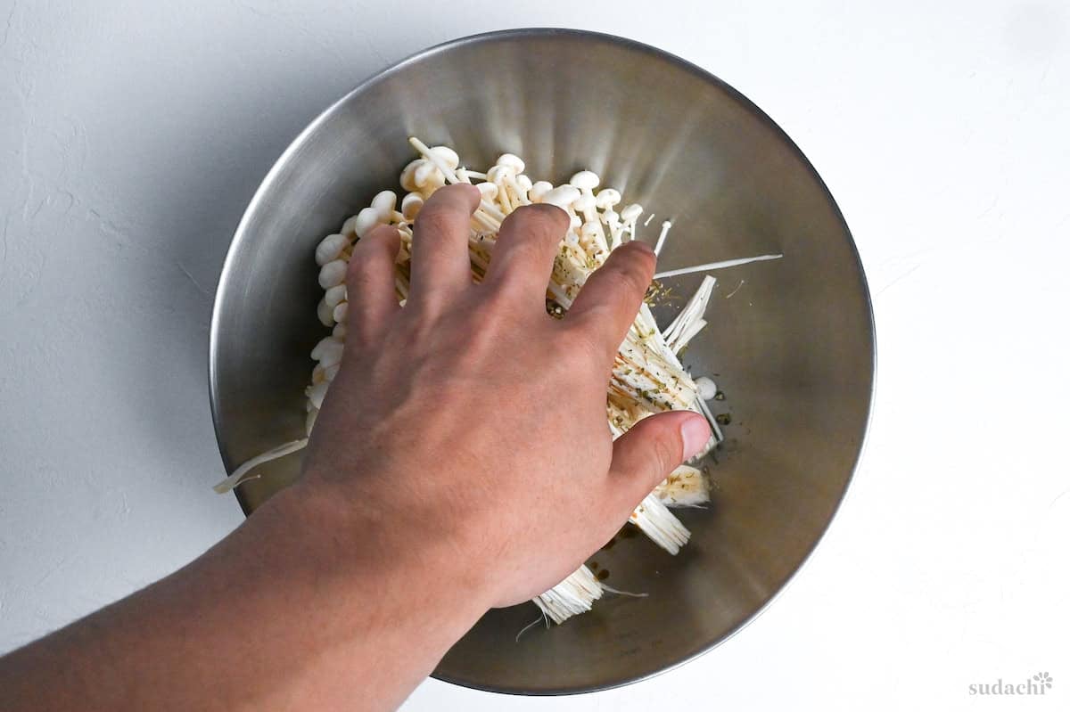 rubbing enoki mushrooms with mixed herbs in a mixing bowl