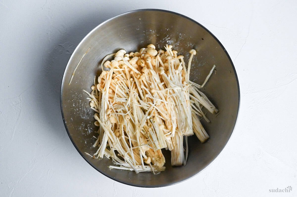 enoki mushrooms coated with potato starch in a mixing bowl on a white background