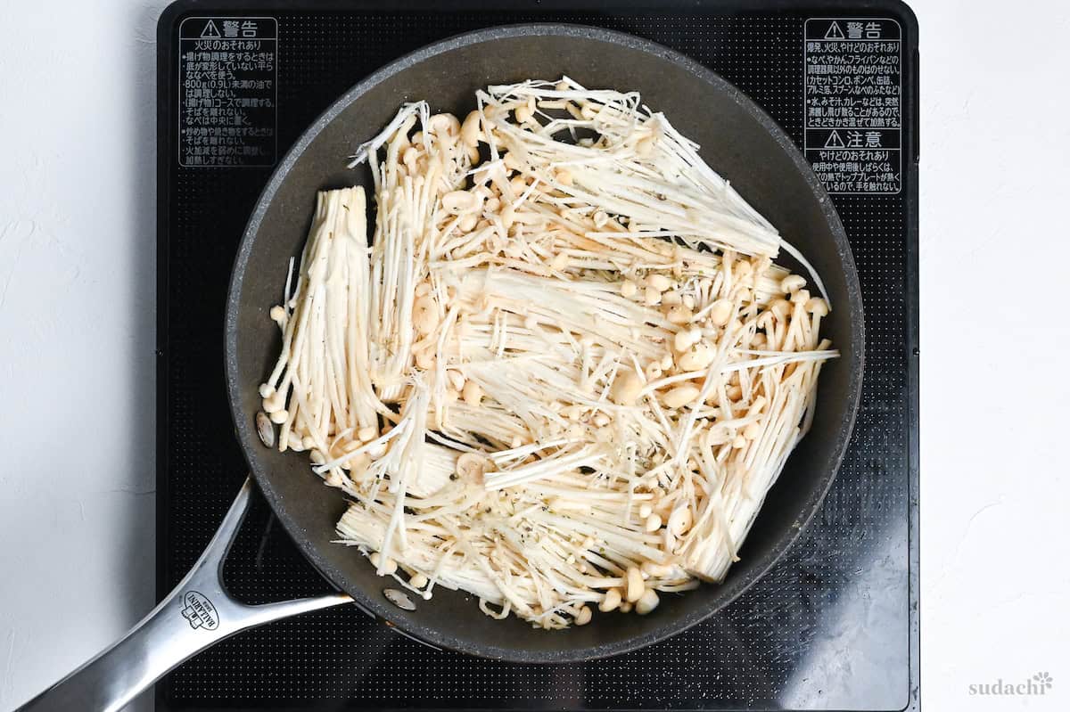 starch dusted enoki mushrooms arranged in a single layer in a frying pan on the stove top