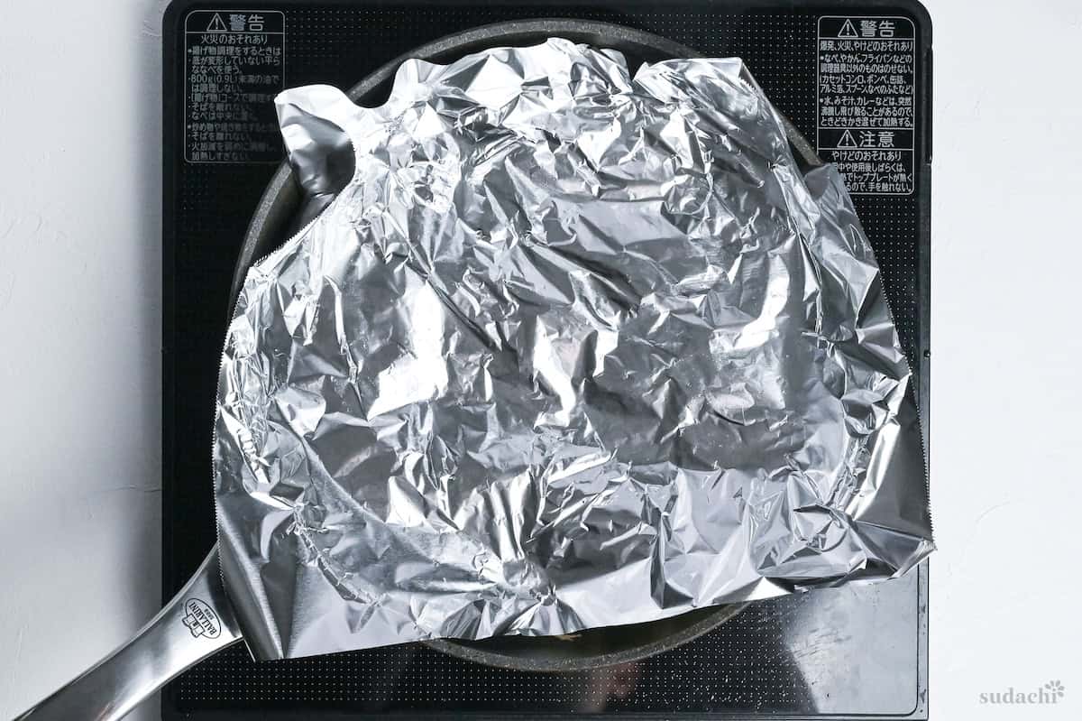 enoki mushrooms in a pan topped with a piece of foil