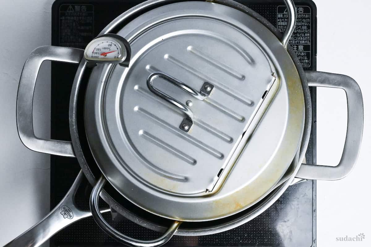 a heavy pot placed over enoki mushrooms in a frying pan to help them crisp up