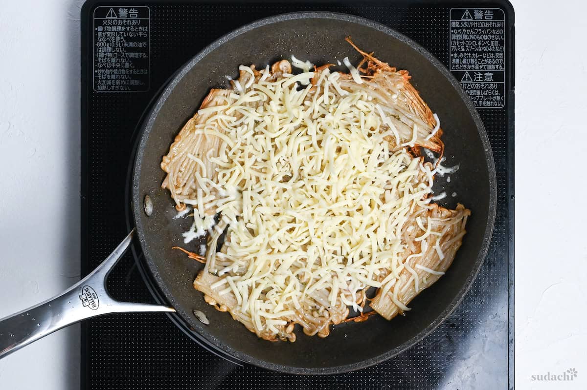 cheese sprinkled over crispy pan-fried enoki mushrooms in a frying pan on the stove