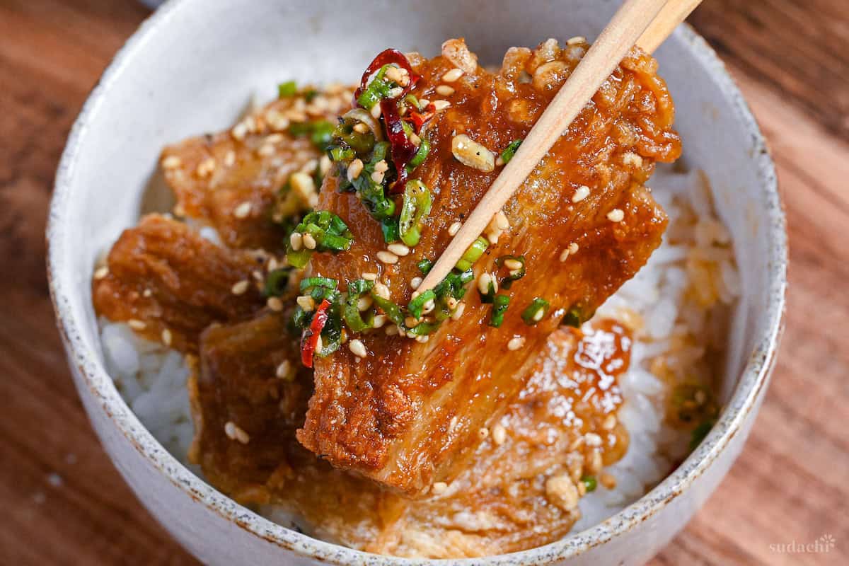 Close up of sauce coated crispy enoki mushrooms held up with wooden chopsticks