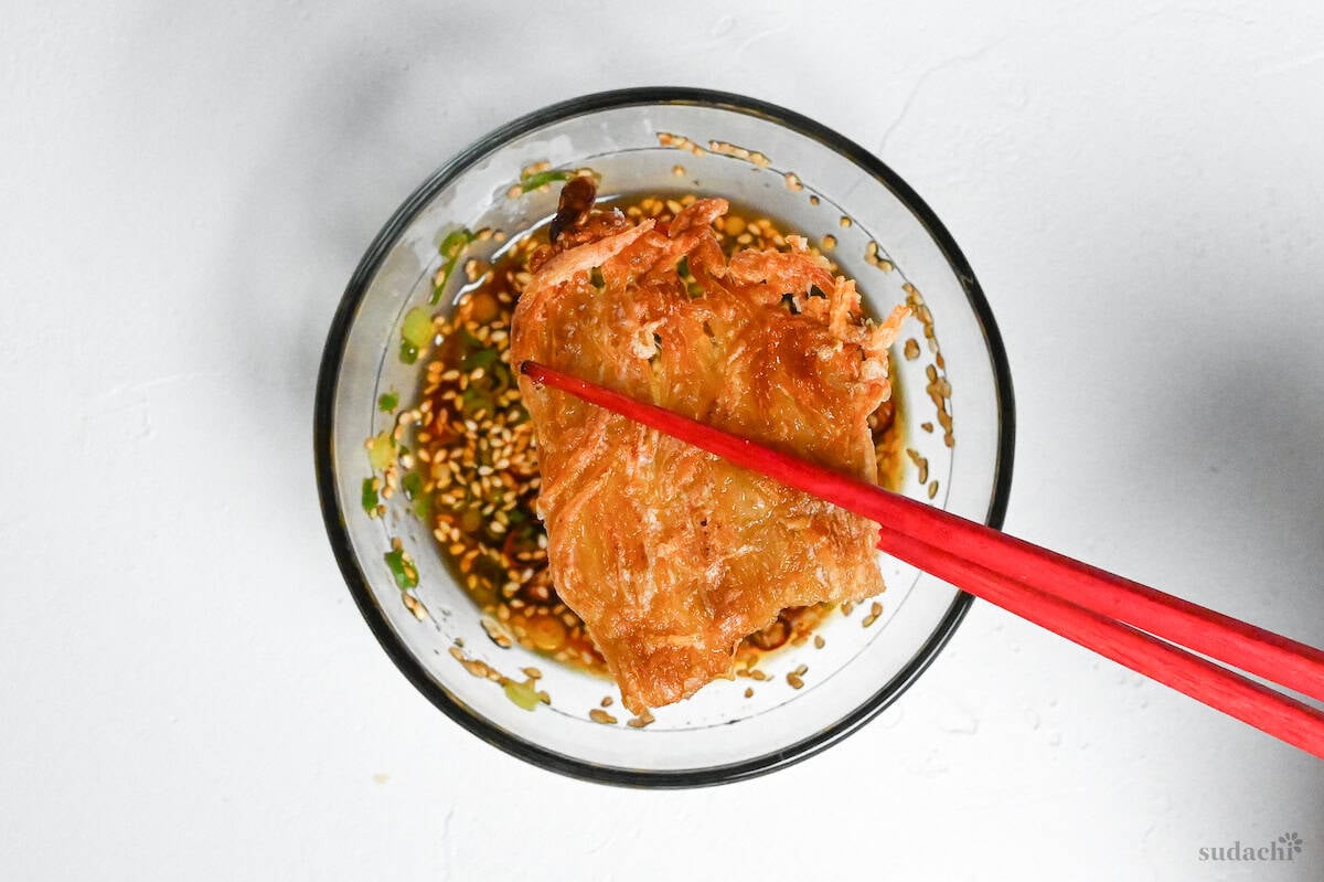 holding crispy fried enoki mushrooms with red chopsticks over bowl of sauce