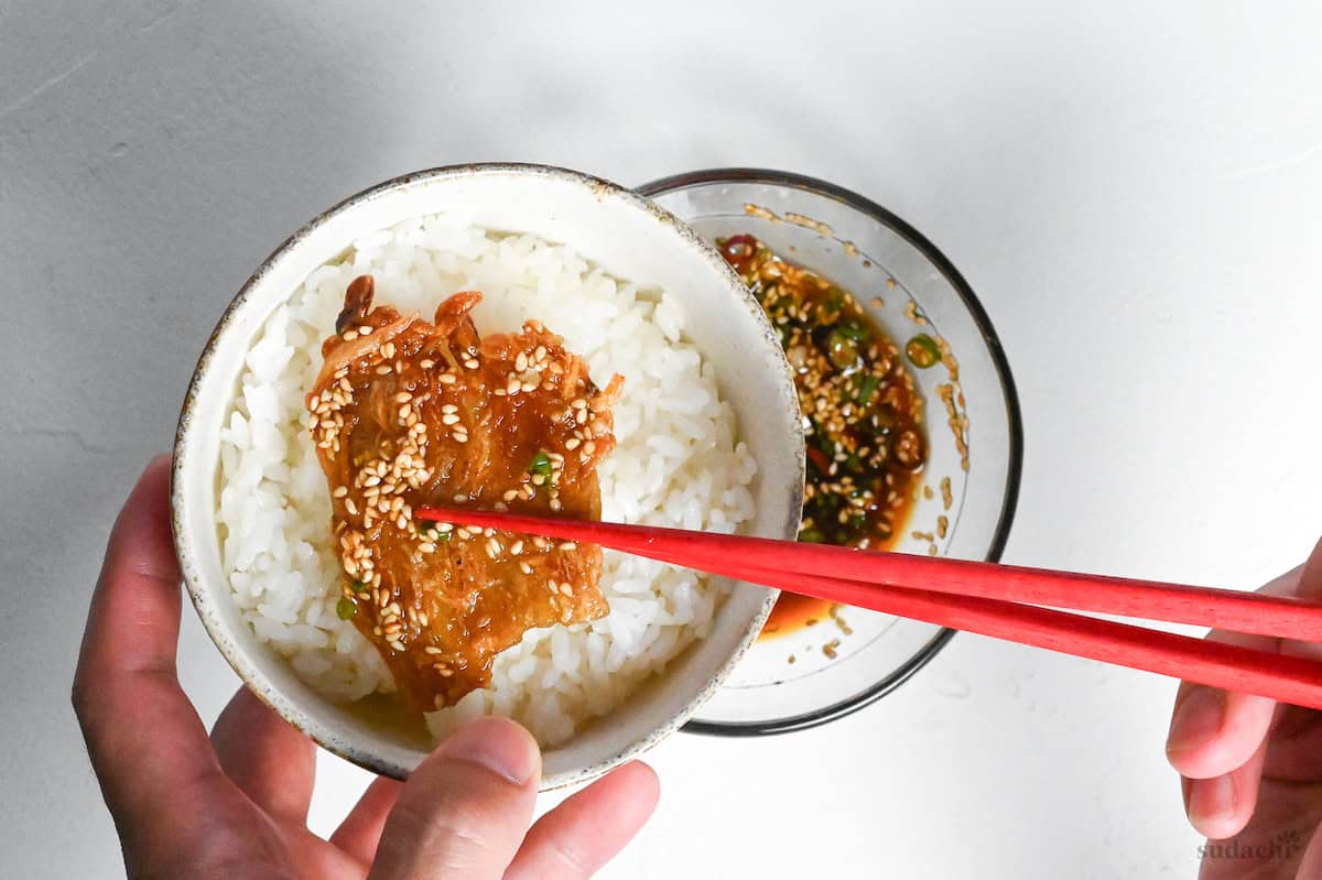 sauce coated crispy enoki mushrooms being placed over rice to make enoki rice bowl