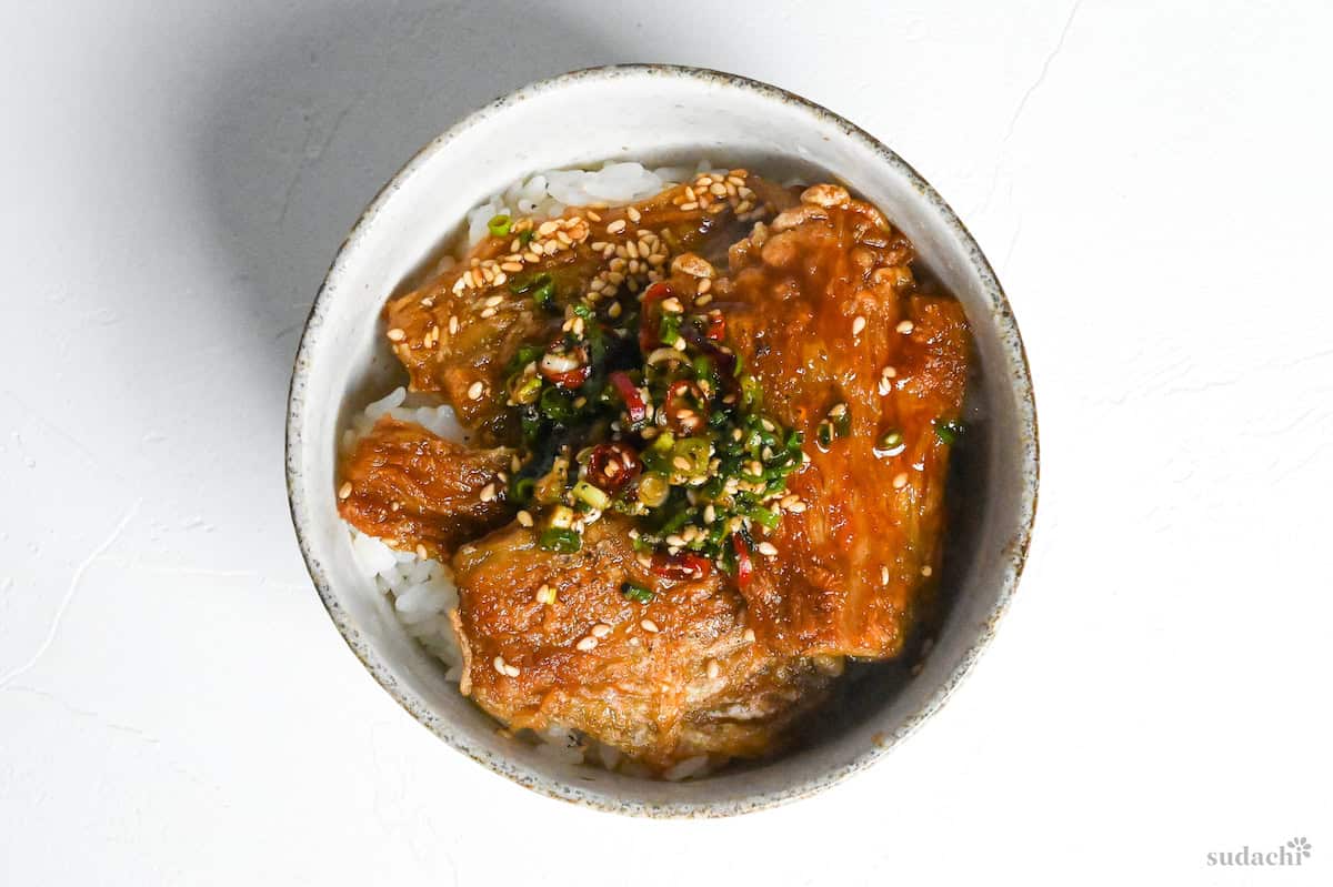 Crispy enoki mushroom rice bowl topped with green onions, sesame seeds and dried red chilis in an off white bowl on a white background