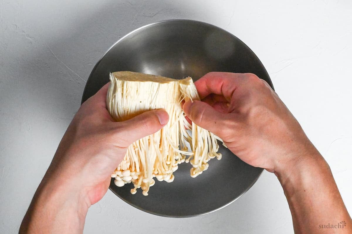tearing enoki mushrooms into a mixing bowl