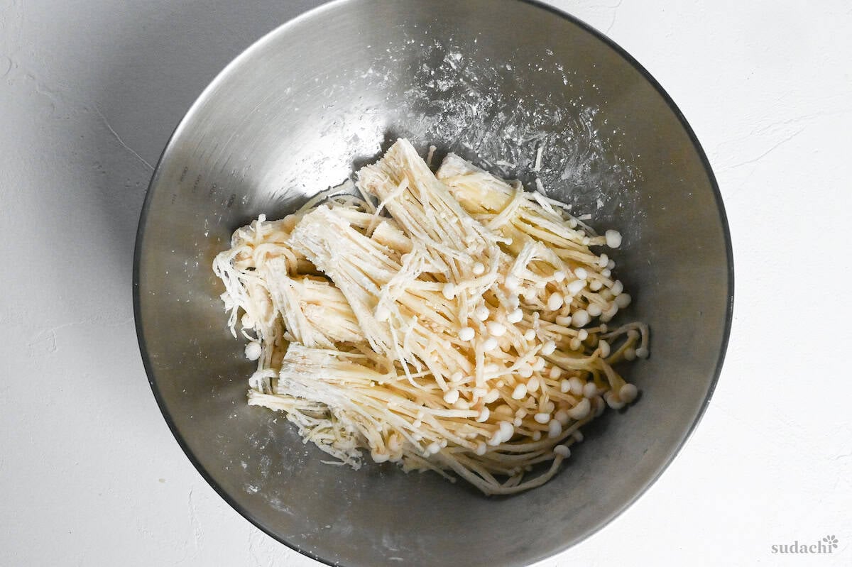 small bunches of enoki mushrooms coated with oil and starch in a mixing bowl