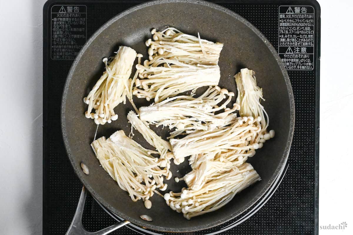 bunches of starch-coated enoki mushrooms frying in a pan